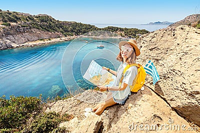 Tourist student with map and greek flag standing on top of the hill at background of the inspirational blue lagoon bay. Solo Editorial Stock Photo