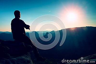 Tourist take a rest. Handsome young man sitting on the rock and enjoying view into misty rocky mountains. Stock Photo