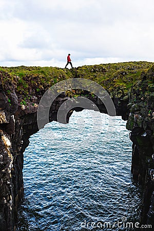 Tourist walks over a natural rock bridge in Arnarstapi, Iceland Stock Photo