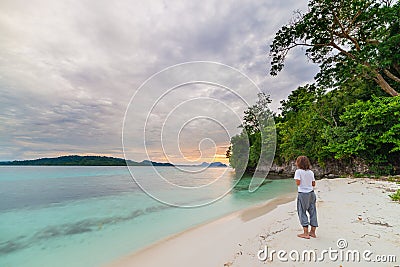 Tourist watching a relaxing sunset sitting on the beach in the remote Togean Islands, Central Sulawesi, Indonesia, upgrowing Stock Photo