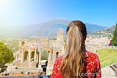 Tourist woman in Italy. Back view of girl visiting Greek theather of Taormina with Etna volcano on the background, Sicily Stock Photo