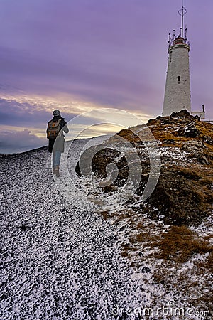 Tourist woman with photographer backpack doing to the lighthouse in Reykjanes Peninsula Reykjanesviti Stock Photo