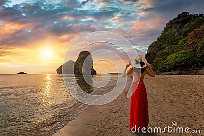 A tourist woman in a red dress stands at the beautiful Phra Nang Cave beach Stock Photo