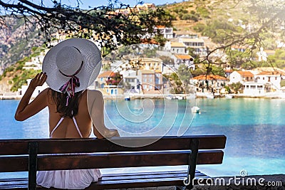 Tourist woman sits on a bench and enjoys the view to the idyllic village of Assos Stock Photo