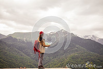 Man Traveler with map and red backpack searching location outdoor with rocky mountains on background Stock Photo