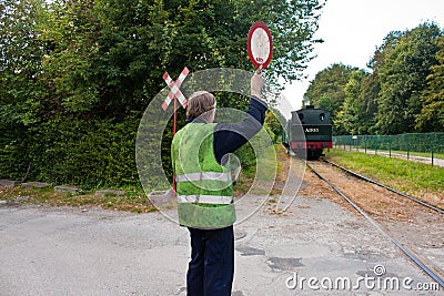 Touristic railway flagman at level crossing stopping car traffic Editorial Stock Photo