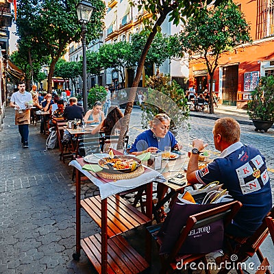 Tourists enjoy at restaurant terrace typically Spanish cuisine, seafood paella with squids, mussels, clams, and prawns Editorial Stock Photo