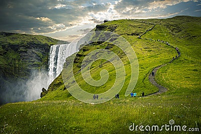 Tourists walking up path with waterfall and green grass in iceland Stock Photo