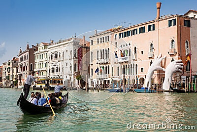 Tourists at a gondola in front of the hands sculpture created by Spanish artist Lorenzo Quinn in the Venice Grand Canal to call at Editorial Stock Photo