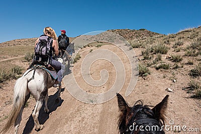 Tourists horse riding through alpine landscape and forest, near Bokonbayevo, Kyrgyzstan Editorial Stock Photo