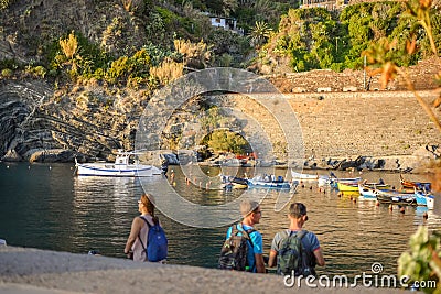 Tourists including a blurred group of young backpackers enjoy a late afternoon at the boat harbor of Vernazza, Italy Editorial Stock Photo