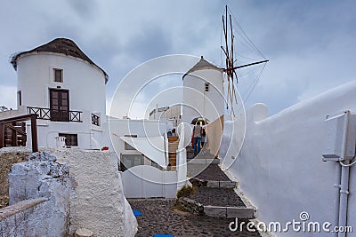 Tourists near windmill in the colorful village of Oia on a rainy day Stock Photo