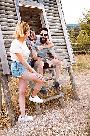 Tourists relaxing. Group of three friends sitting on wooden camp stairs enjoying and laughing in the countryside. Camp adventure Stock Photo