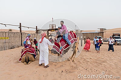 Tourists Riding Camel with Tamer in The Desert of Dubai Editorial Stock Photo