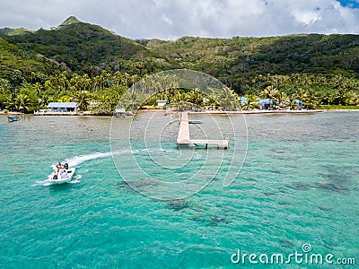 Tourists riding high speed jet boat in a stunning azure blue turquoise lagoon. Aerial view. Raiatea, French Polynesia. Stock Photo