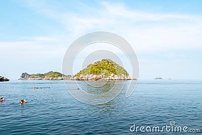 Tourists are snorkeling in the ocean with rocks with vegetation underneath beautiful blue sky with clouds Editorial Stock Photo