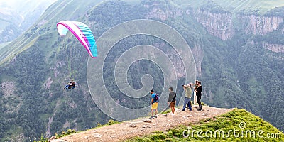 Tourists on top of a mountain pass, taking pictures of a flying paraglider Editorial Stock Photo