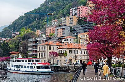 Tourists walk on a lakeside promenade under beautiful blossoming trees by Lake Como in Lombardy Italy Editorial Stock Photo
