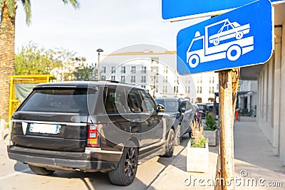 Tow-away zone sign is hanging on a pole at the curb on city street, but the SUV is still parked near it in the wrong Editorial Stock Photo