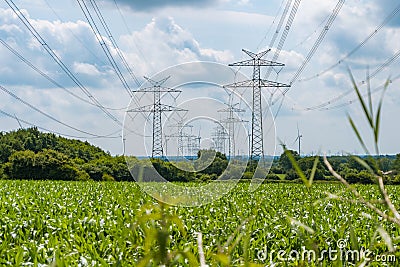 Towers with multiple power lines over a green field with blue sky Stock Photo