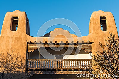 Towers of an old pueblo style adobe building with rustic, ornate wood beams and balcony in Santa Fe, New Mexico Stock Photo