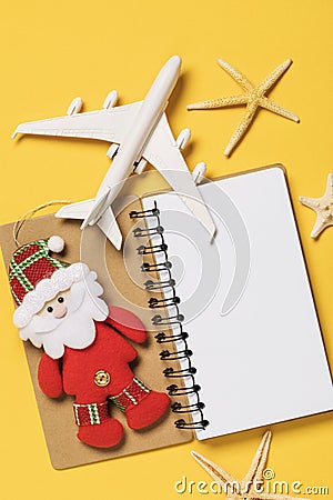 Toy airplane, Santa Claus and notebook on a yellow background with copy space. Christmas travel planning concept Stock Photo