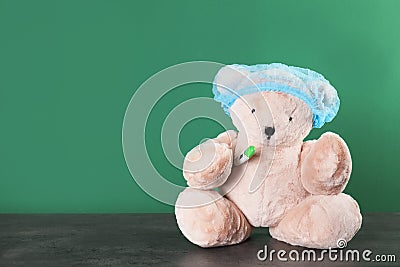 Toy bear with thermometer on table against color background. Children`s hospital Stock Photo
