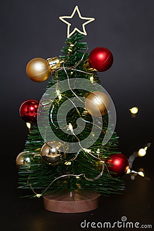 Toy christmas tree with balls on a black background with a garland. Cute Stock Photo