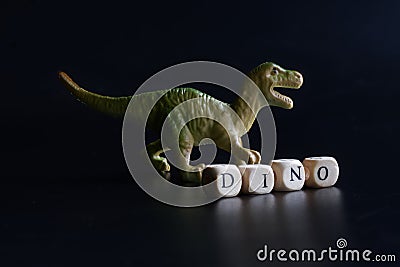 Toy dinosaur that looks like a Tyrannosaurus, Velociraptor, Allosaurus, Megalosaurus or Plateosaurus stands against a dark Stock Photo