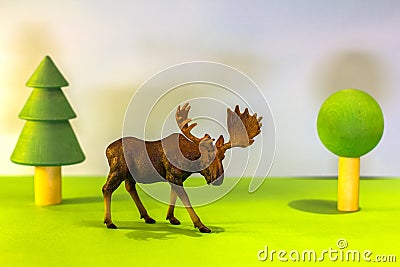 Toy elk in a toy forest. like a real moose on a bright studio background with wooden trees. Eco toys. Stock Photo