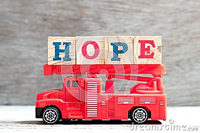 Toy fire ladder truck hold block in word hope on wood background Stock Photo