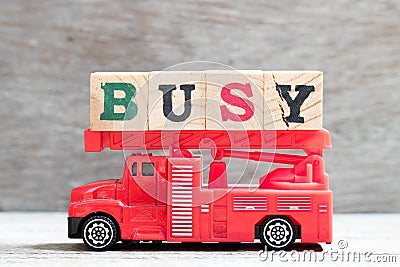 Toy fire ladder truck hold block in word busy on wood background Stock Photo