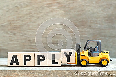 Toy forklift hold letter block y to complete word apply on wood background Stock Photo