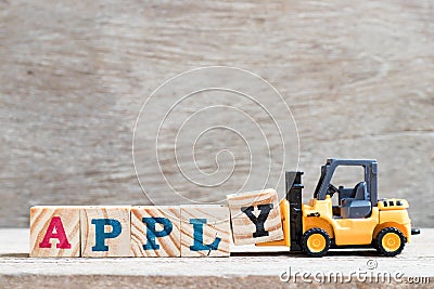 Toy forklift hold block y to complete word apply on wood background Stock Photo