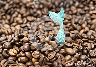 Toy mermaid tail sticks out of a pile of roasted coffee beans Stock Photo