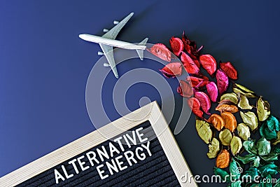 Toy passenger airliner with a contrail of multi-colored flower petals next to the inscription alternative energy. Concept of eco- Stock Photo