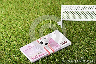 Toy soccer ball and euro banknotes near miniature football gates on green grass Stock Photo