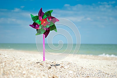 Toy windmill close-up on the background of sand of the sea and sky, children`s game toy colored blades pinwheel weather vane Stock Photo