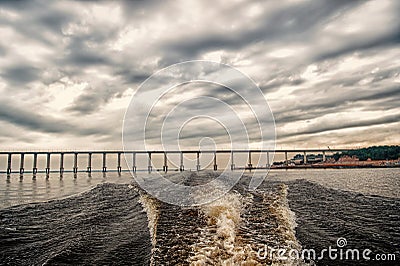 Trace of speed boat on blue sea water in manaus, brazil. Seascape with bridge on horizon on cloudy sky. travelling and Stock Photo