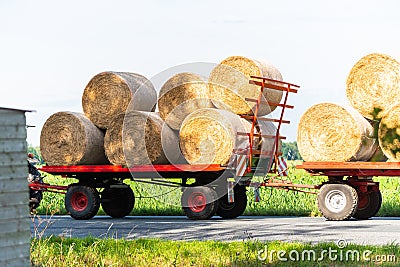 A tractor drives with two trailers and some hay bales on a country road Stock Photo