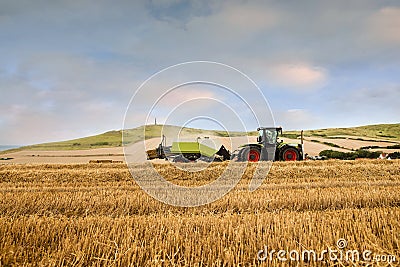 tractor equipped with a baler picking up the straw to make large rectangular bales before the rain Editorial Stock Photo