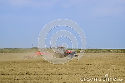 Tractor with a grader aligns the soil on the field. The tractor raised dust. Editorial Stock Photo