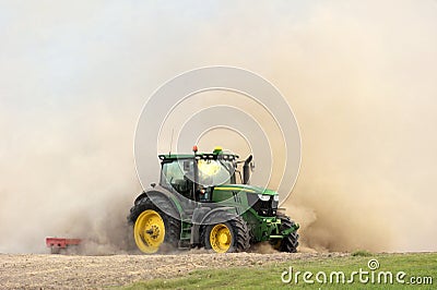 The tractor harrows the field in a huge dust cloud. Stock Photo