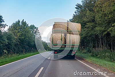 tractor loaded with several straw bales drives over a country road Stock Photo