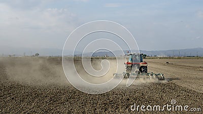 Tractor plowing a dusty field with unrecognizable people Stock Photo