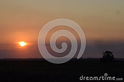 Tractor plowing plow the field on a background sunset. tractor silhouette on sunset background Stock Photo