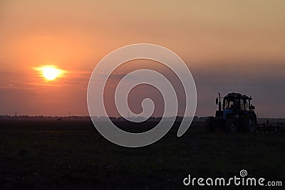 Tractor plowing plow the field on a background sunset. tractor silhouette on sunset background Stock Photo