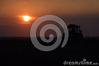 Tractor plowing plow the field on a background sunset. tractor silhouette on sunset background Stock Photo