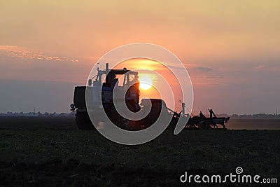Tractor plowing plow the field on a background sunset. tractor silhouette on sunset background Stock Photo