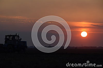 Tractor plowing plow the field on a background sunset. tractor silhouette on sunset background Stock Photo